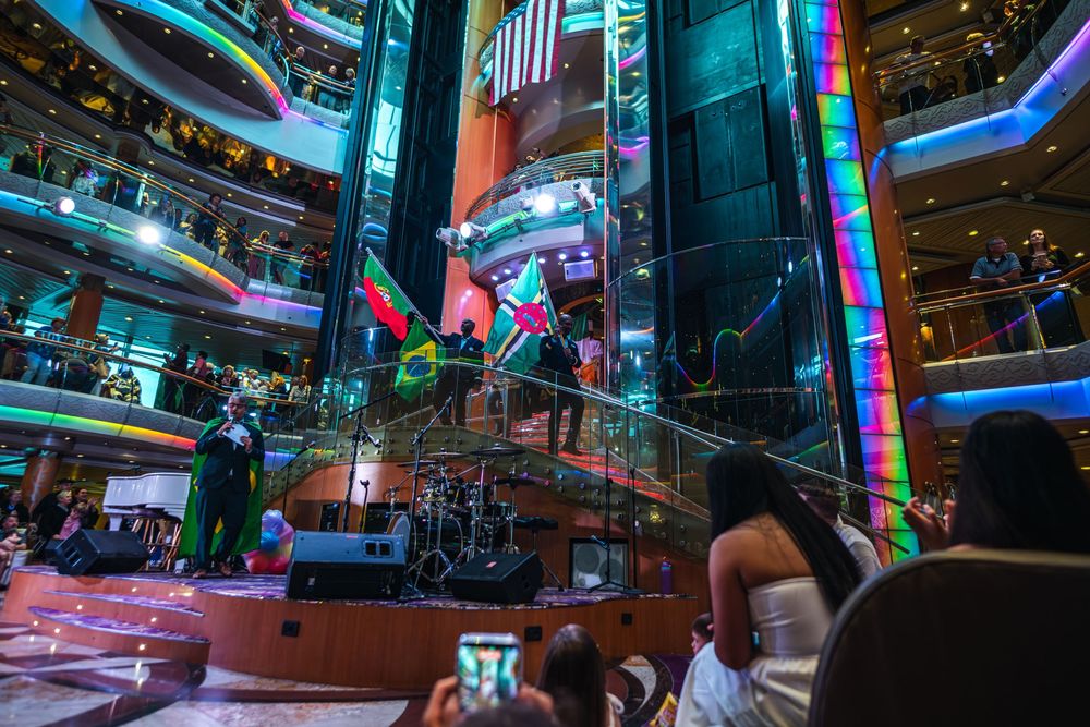 Live band performs in a vibrant cruise ship atrium with colorful lights and guests watching from multiple decks.
