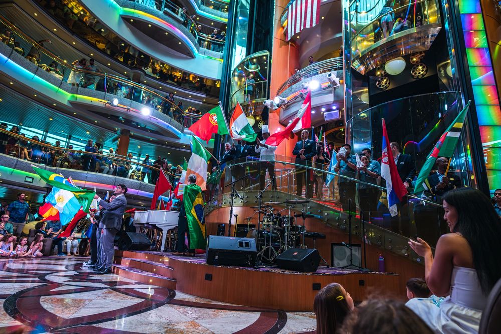 Colorful international flags displayed in a grand cruise ship atrium during a lively multicultural celebration event.
