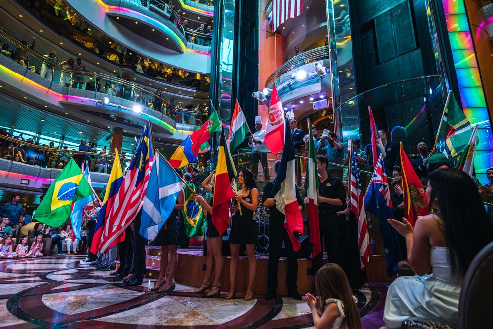 People holding international flags in a colorful atrium during a multicultural ceremony or international event.