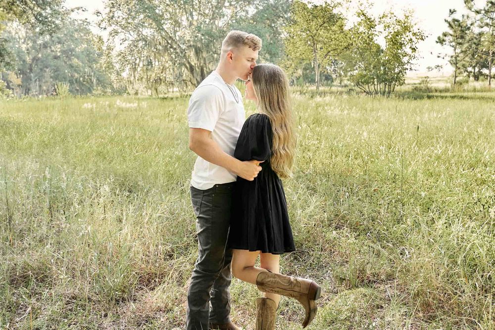 Couple embracing and almost kissing in a lush green field during golden hour in a romantic outdoor setting.
