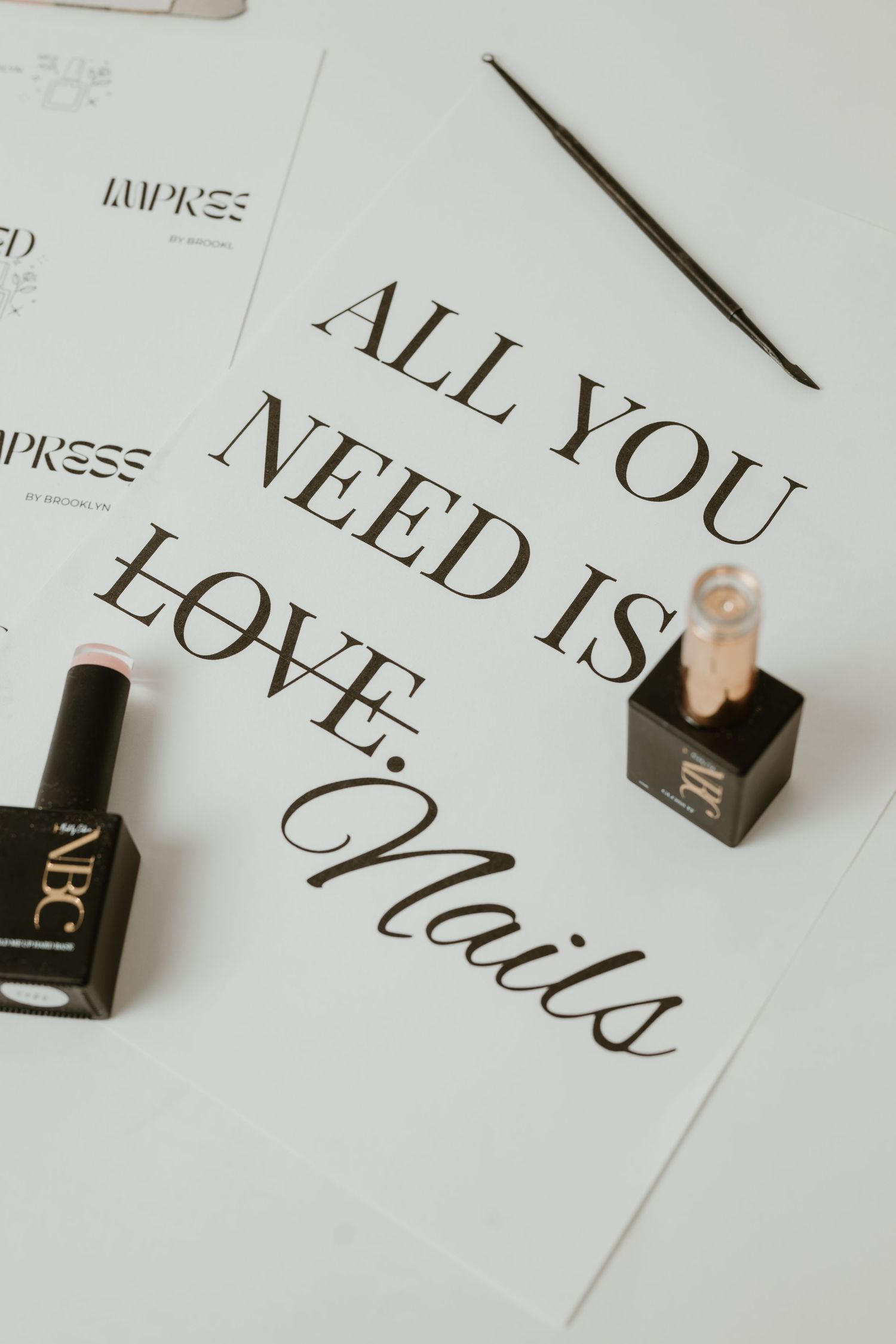 Nail salon flat lay with gel polish bottles, a pen, and a sign reading All You Need Is Love Nails on white background.
