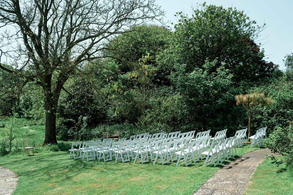 White chairs arranged in rows on a lush green garden lawn for an outdoor wedding ceremony.