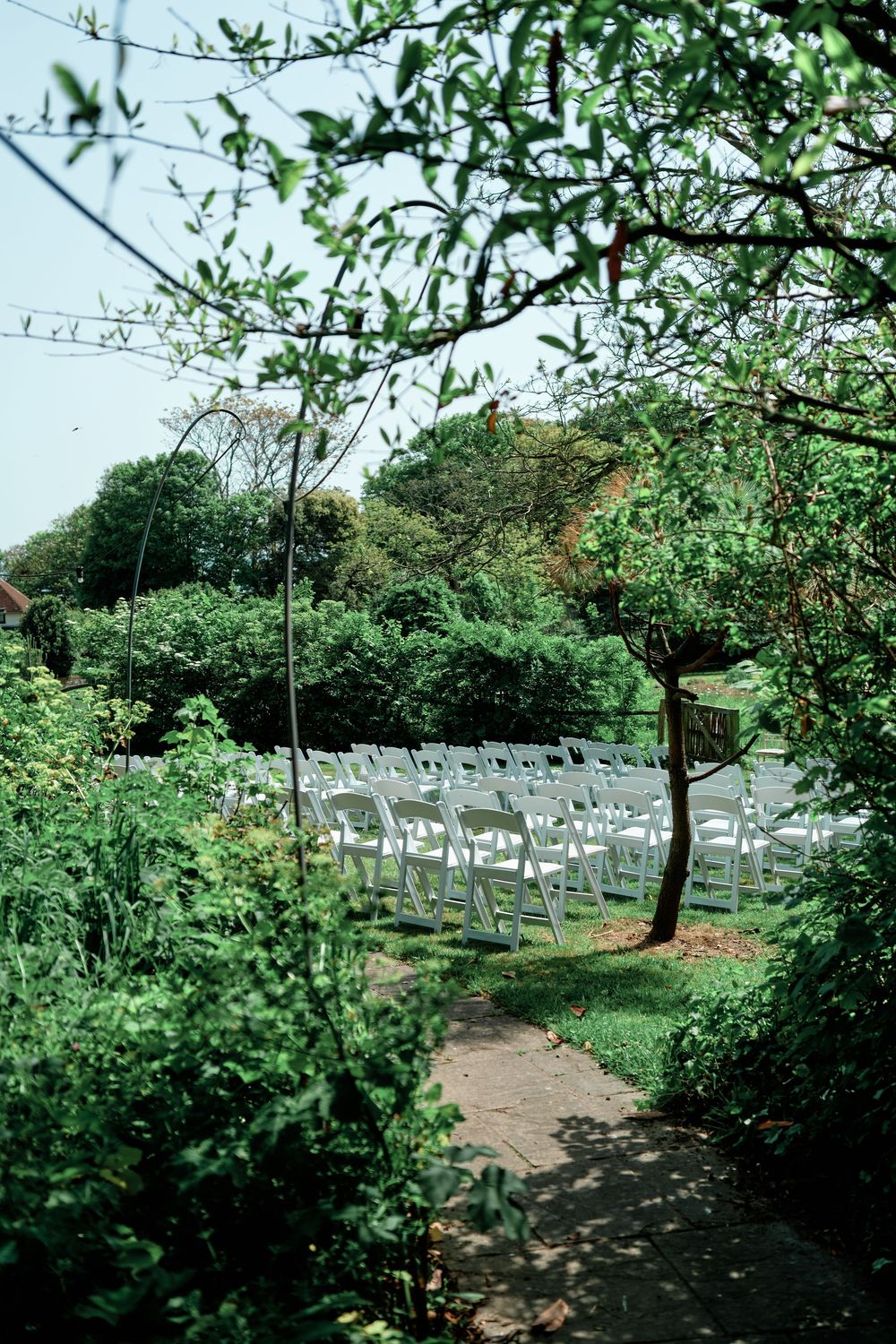 Rows of white folding chairs set up in a lush garden for an outdoor wedding ceremony surrounded by greenery.