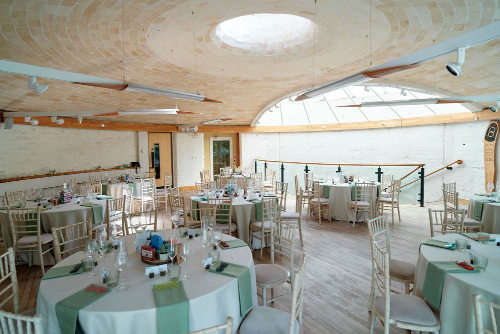 Elegant wedding reception venue with round tables, white linens, sage green napkins, and a wooden vaulted ceiling with skylight.