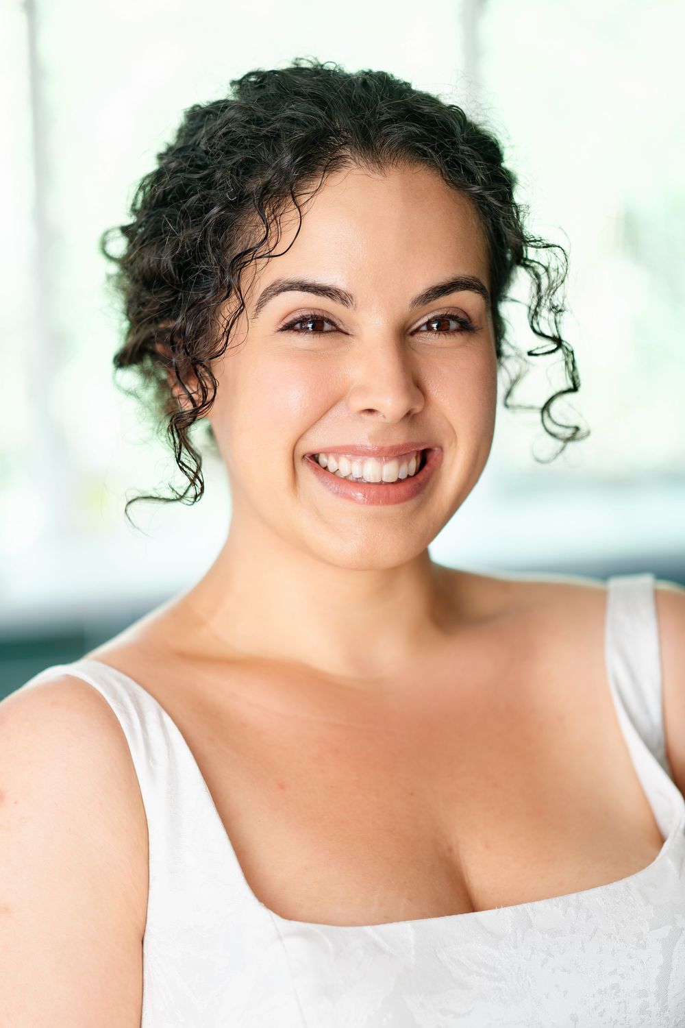 Smiling young woman with curly dark hair wearing a white top, portrait photo.