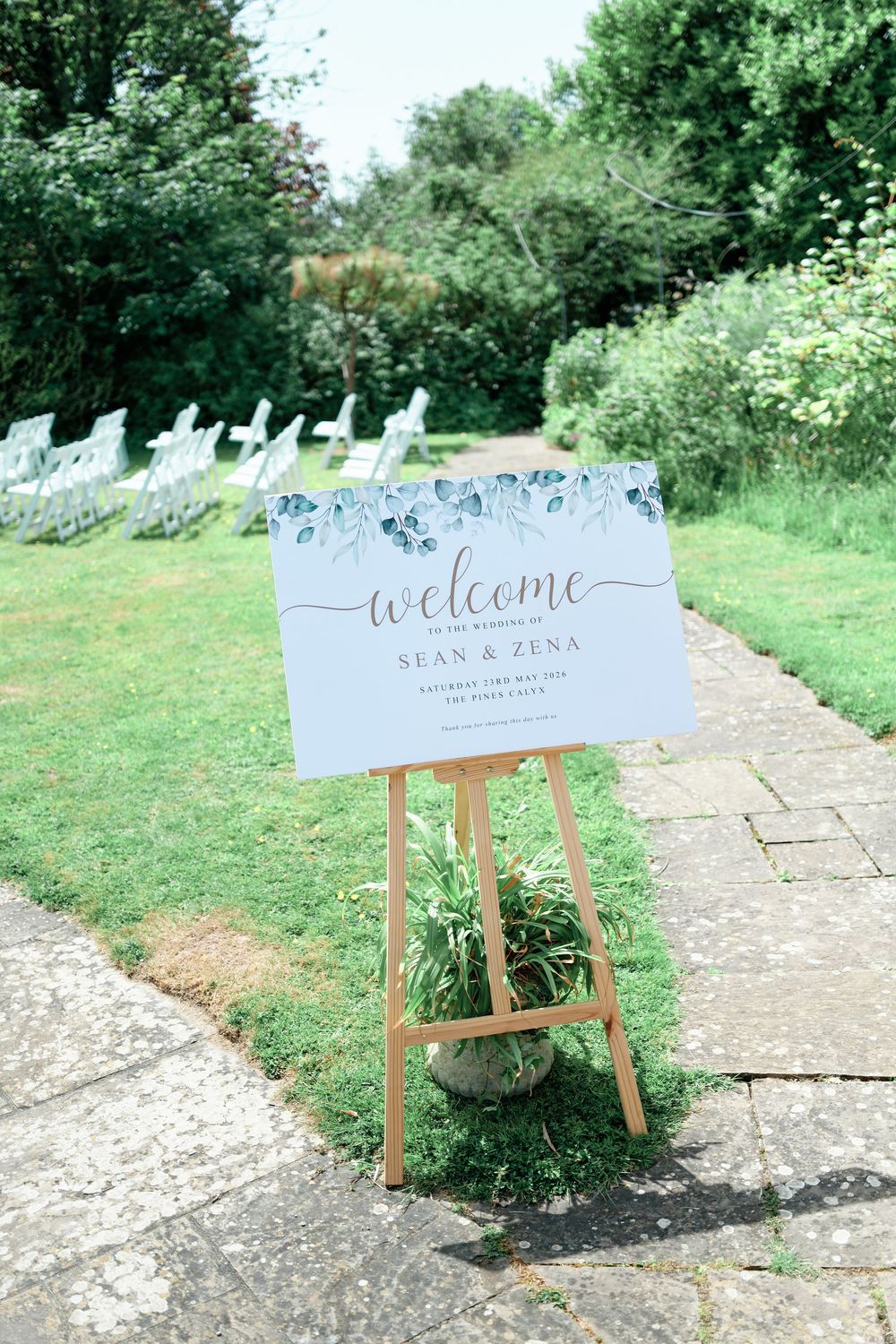 Elegant outdoor wedding welcome sign for Sean and Zena on a wooden easel, adorned with blue botanical greenery details.