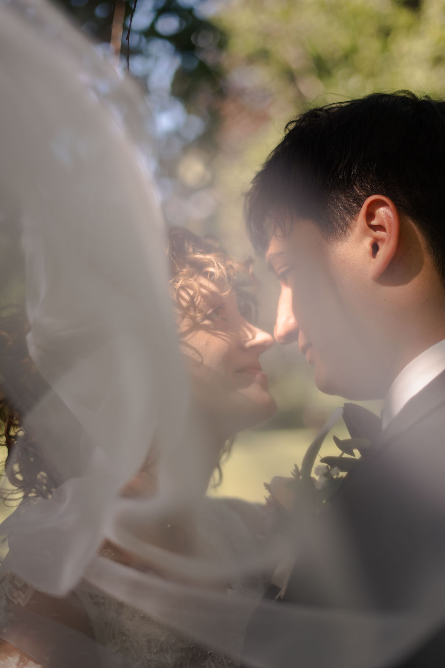 A bride and groom share an intimate moment kissing, softly framed through layers of a flowing white wedding veil.