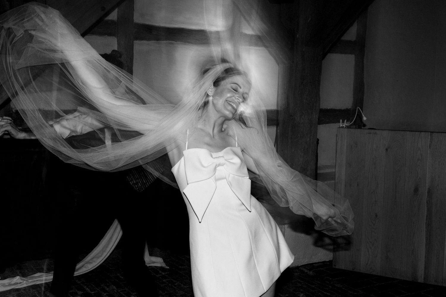 Black and white photo of a bride in a short white dress dancing joyfully with veil flowing.
