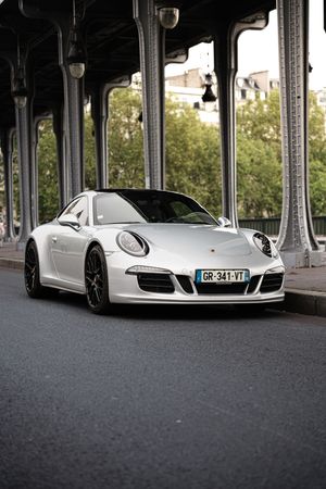 White Porsche 911 parked on a Parisian street under the iconic Bir-Hakeim bridge, France.
