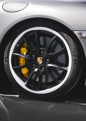 Close-up of Porsche 911 black alloy wheel with yellow brake calipers and Michelin tires.