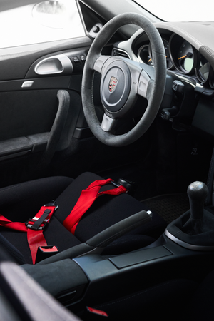 Porsche 911 interior with black sport seats, red racing harness, manual gearbox, and Porsche steering wheel.