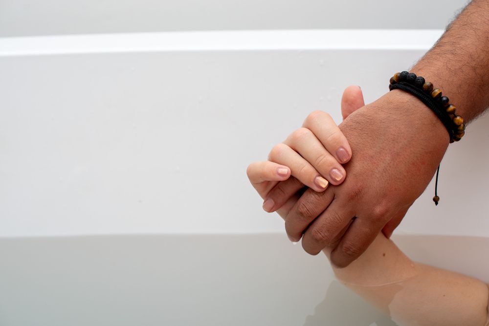 Two hands of different skin tones holding each other tenderly, one wearing a black beaded bracelet.