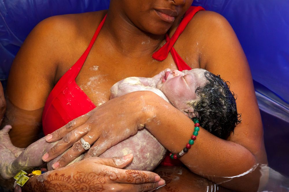 Mother holding her newborn baby covered in vernix immediately after a water birth.