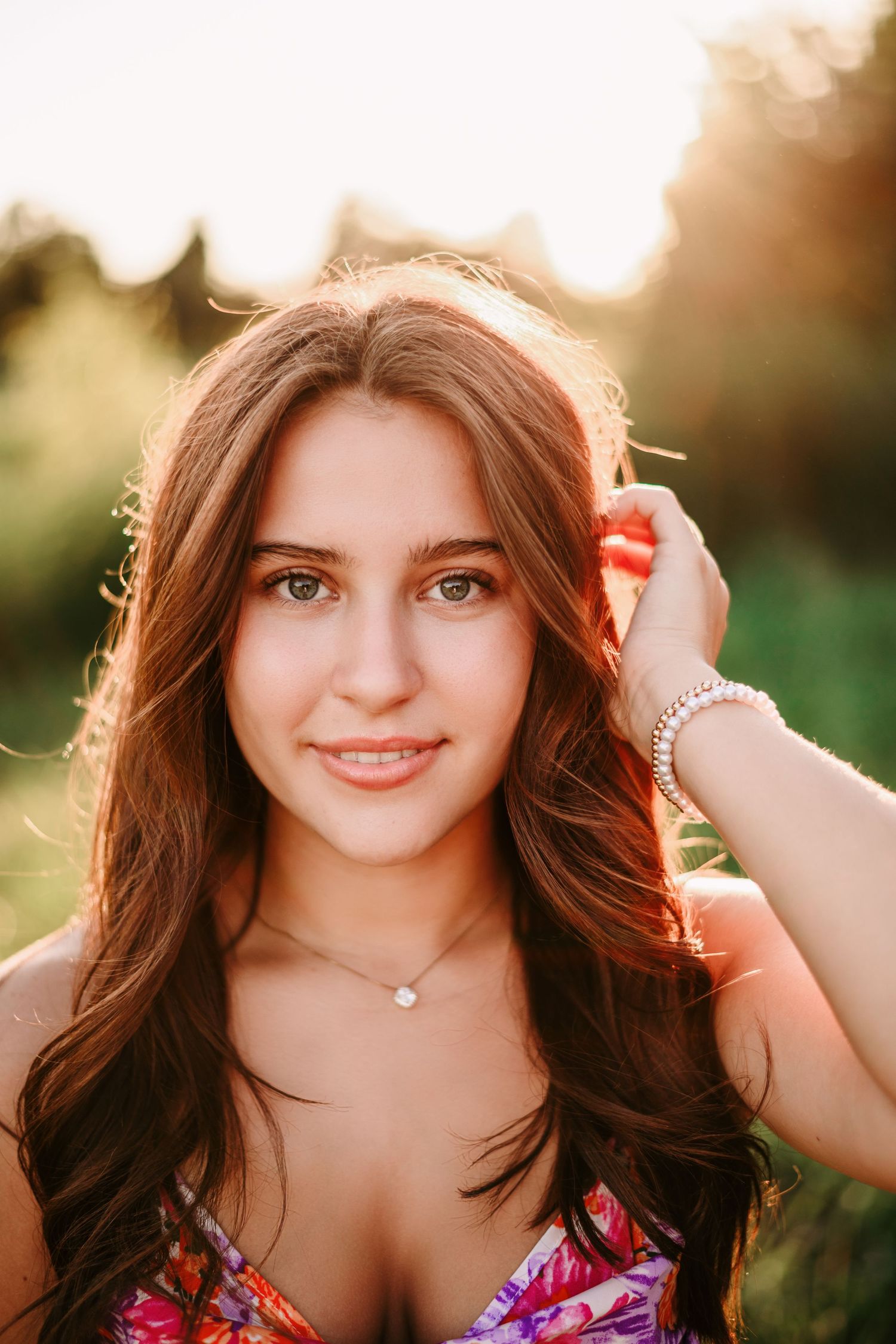 Young blonde woman in light blue dress sitting on blanket in green field during golden hour sunset.