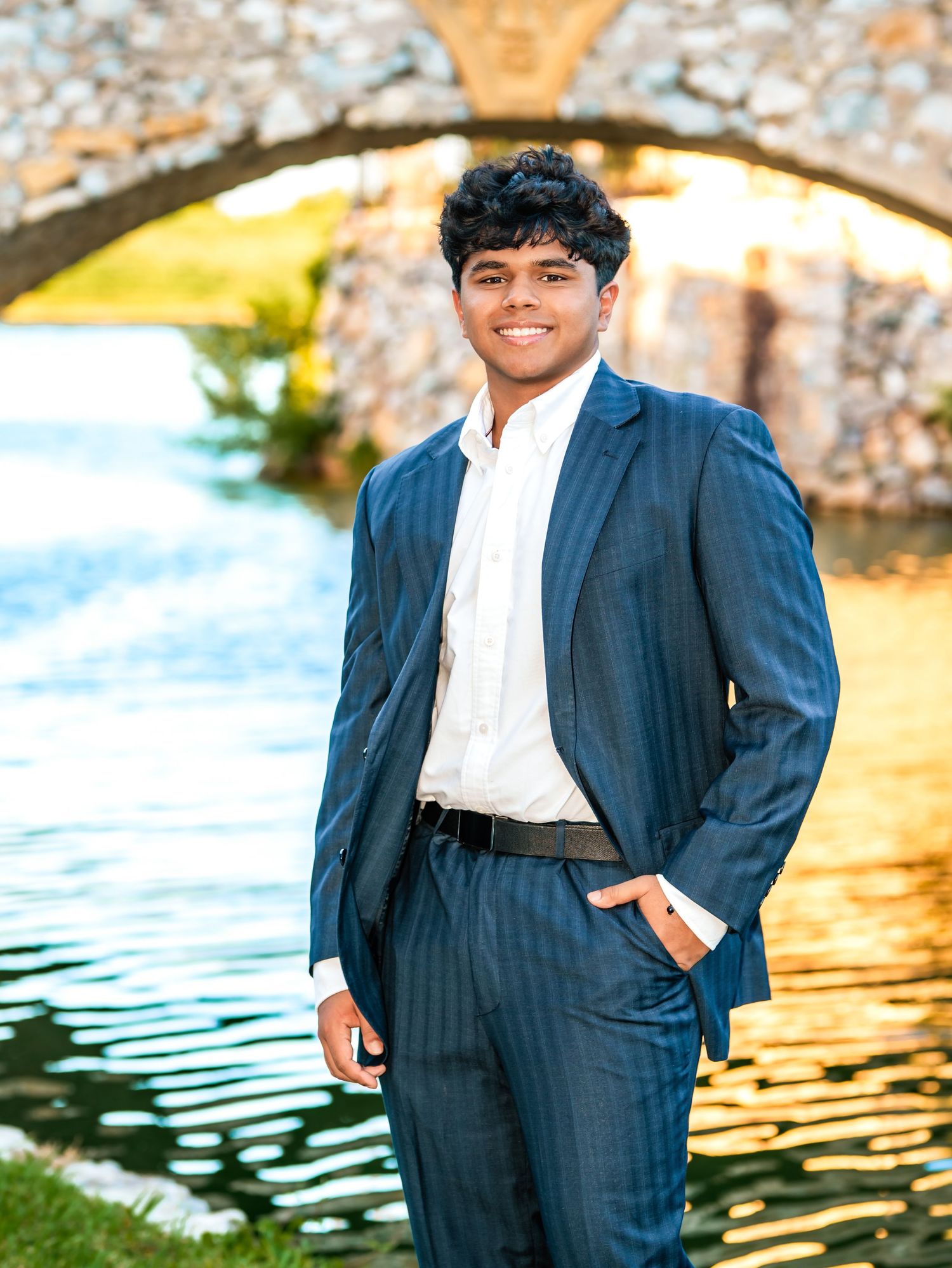 Young man in navy pinstripe suit holding a tennis racket, smiling outdoors in a professional senior portrait.