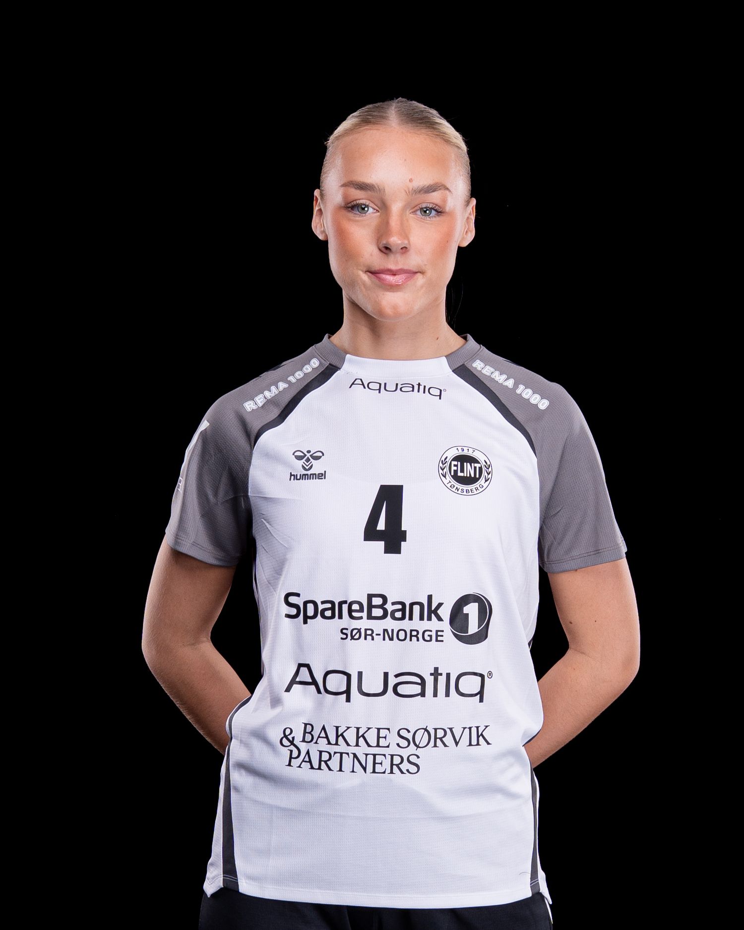 Kvinnelig håndballspiller iført hvit og grå spillertrøye med nummer 4 og sponsorlogoene SpareBank 1 og Aquatiq.