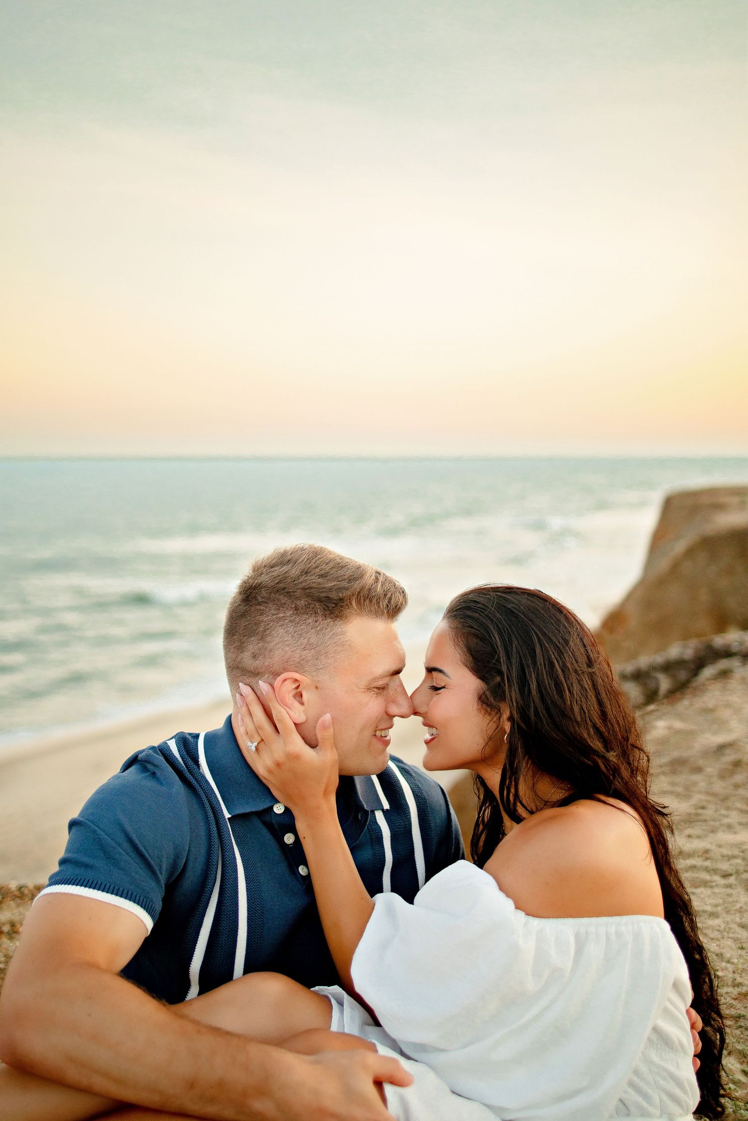 A romantic proposal scene set between rows of grapevines in a scenic vineyard with white flowers and a blanket.