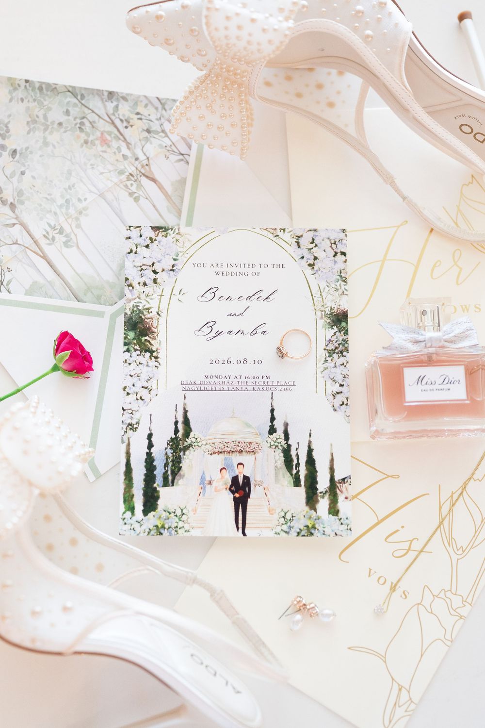 Elegant wedding invitation for Benedict and Byamba surrounded by bridal accessories and perfume.