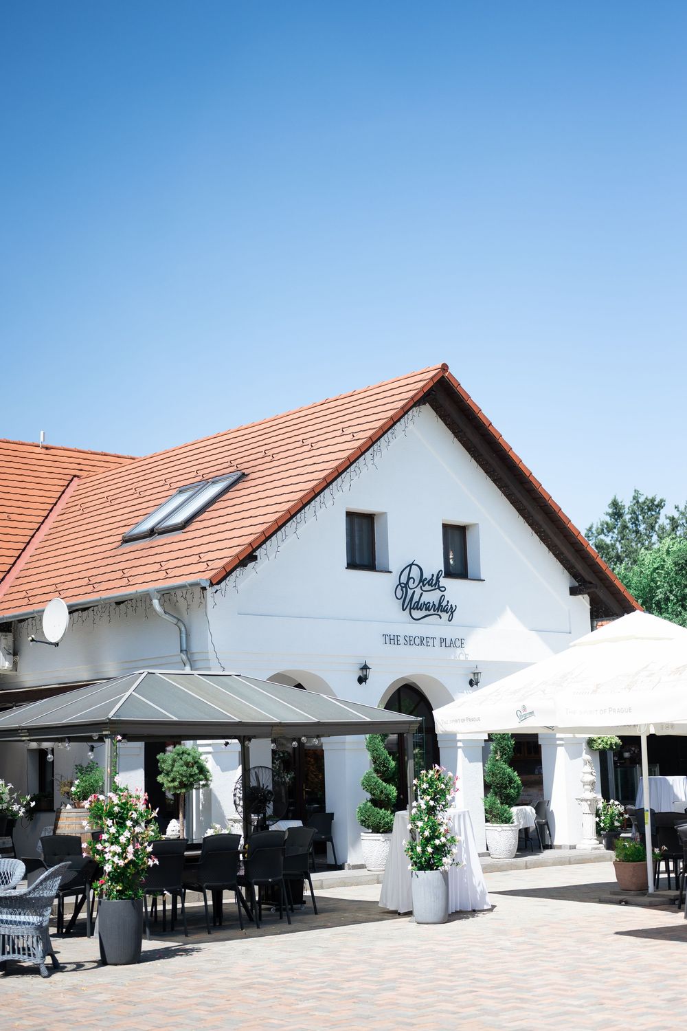 Charming white wedding venue with red roof terrace and outdoor seating under blue sky.