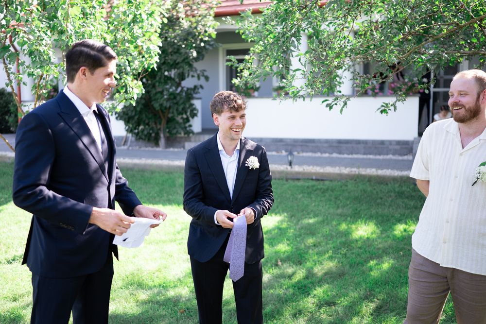 Three men in suits conversing outdoors in a garden during a wedding celebration.