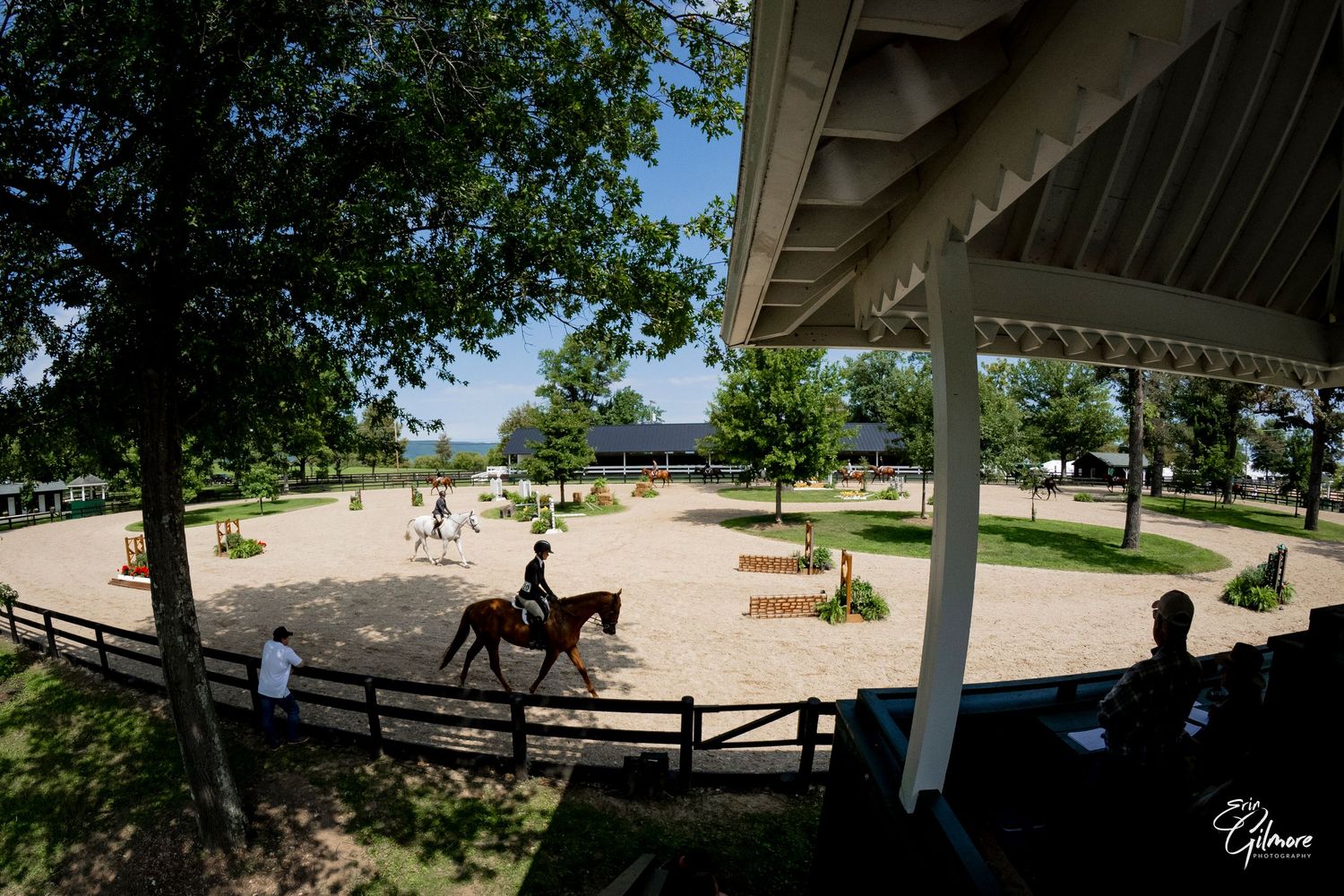 Rider in black jacket jumps a dark horse over a brick fence obstacle at an outdoor equestrian show.