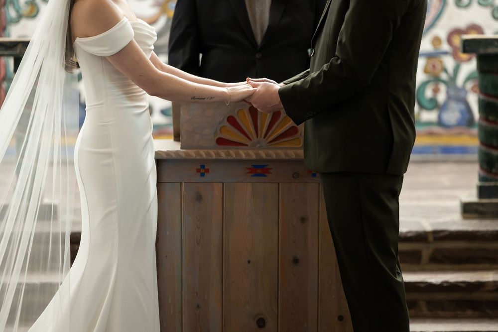 Bride and groom holding hands at wedding altar, bride in elegant white off-shoulder gown with veil.