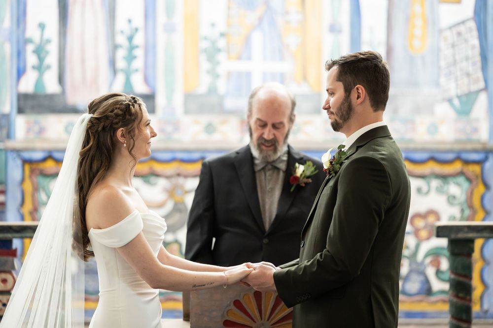 Bride and groom exchange vows holding hands before officiant in ornate tiled chapel during wedding ceremony.