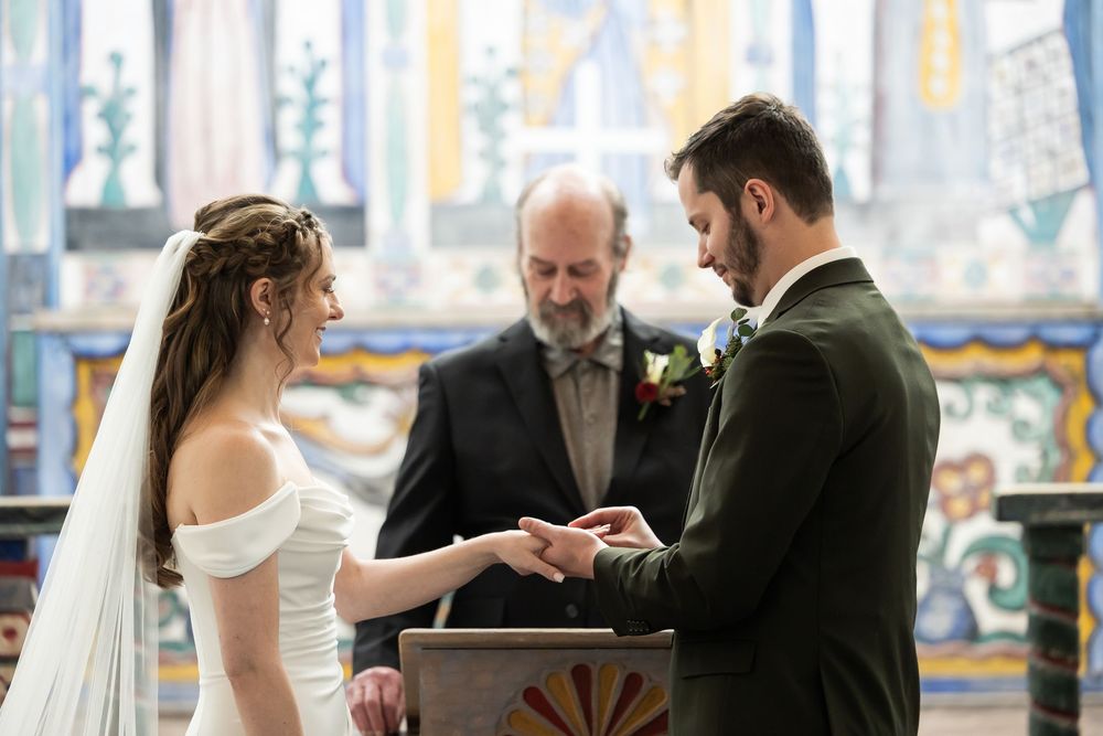 Bride and groom exchange rings at church altar with officiant during elegant wedding ceremony.