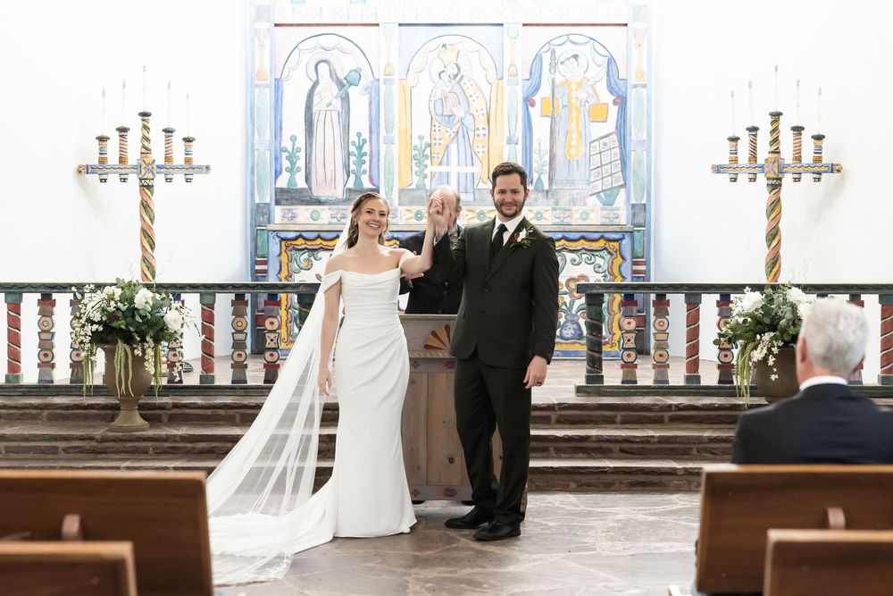 Bride and groom celebrate at church altar with colorful mosaic backdrop and candles during wedding ceremony.