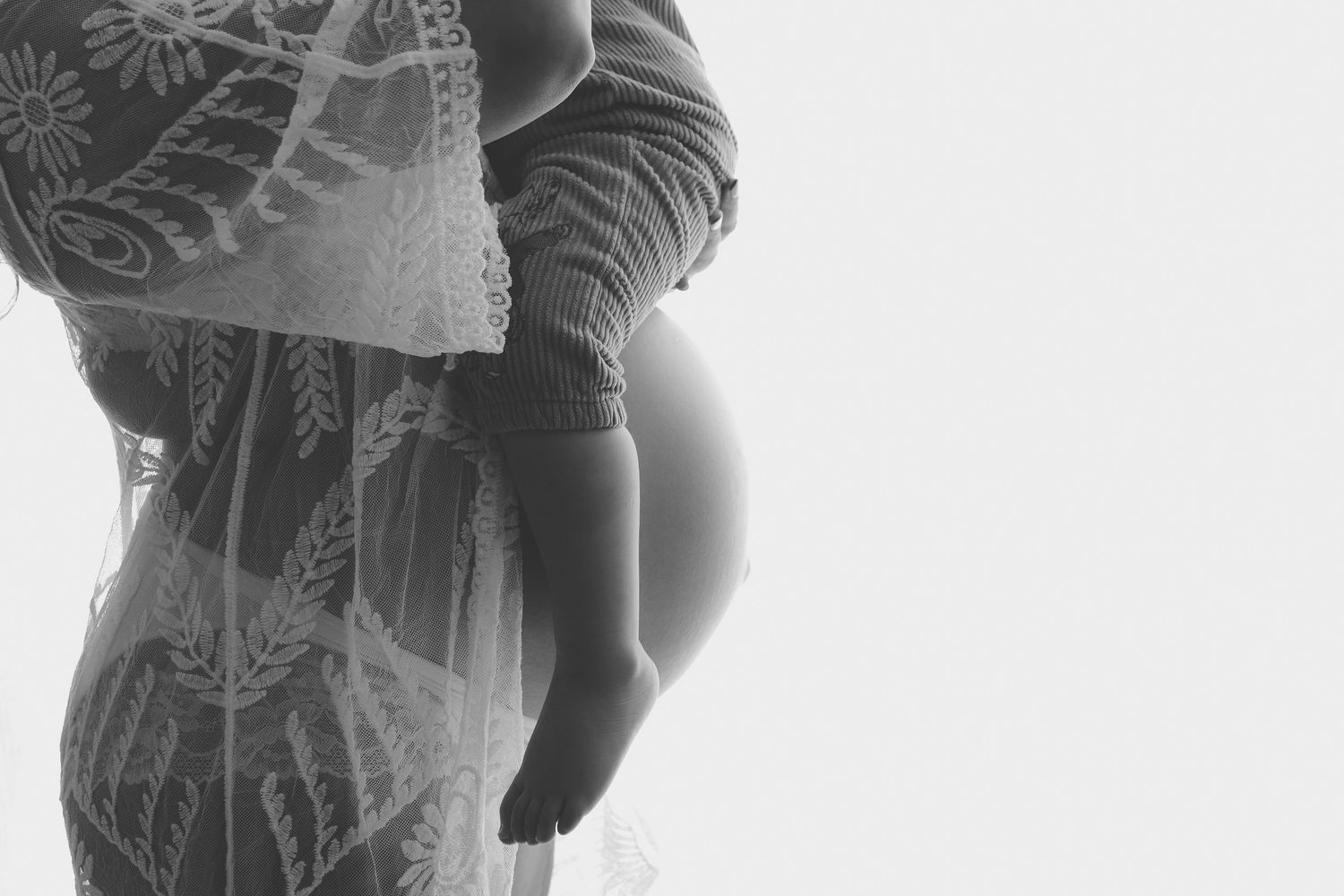 Black and white maternity photo of a pregnant woman in lace robe, showcasing her baby bump in a studio setting.