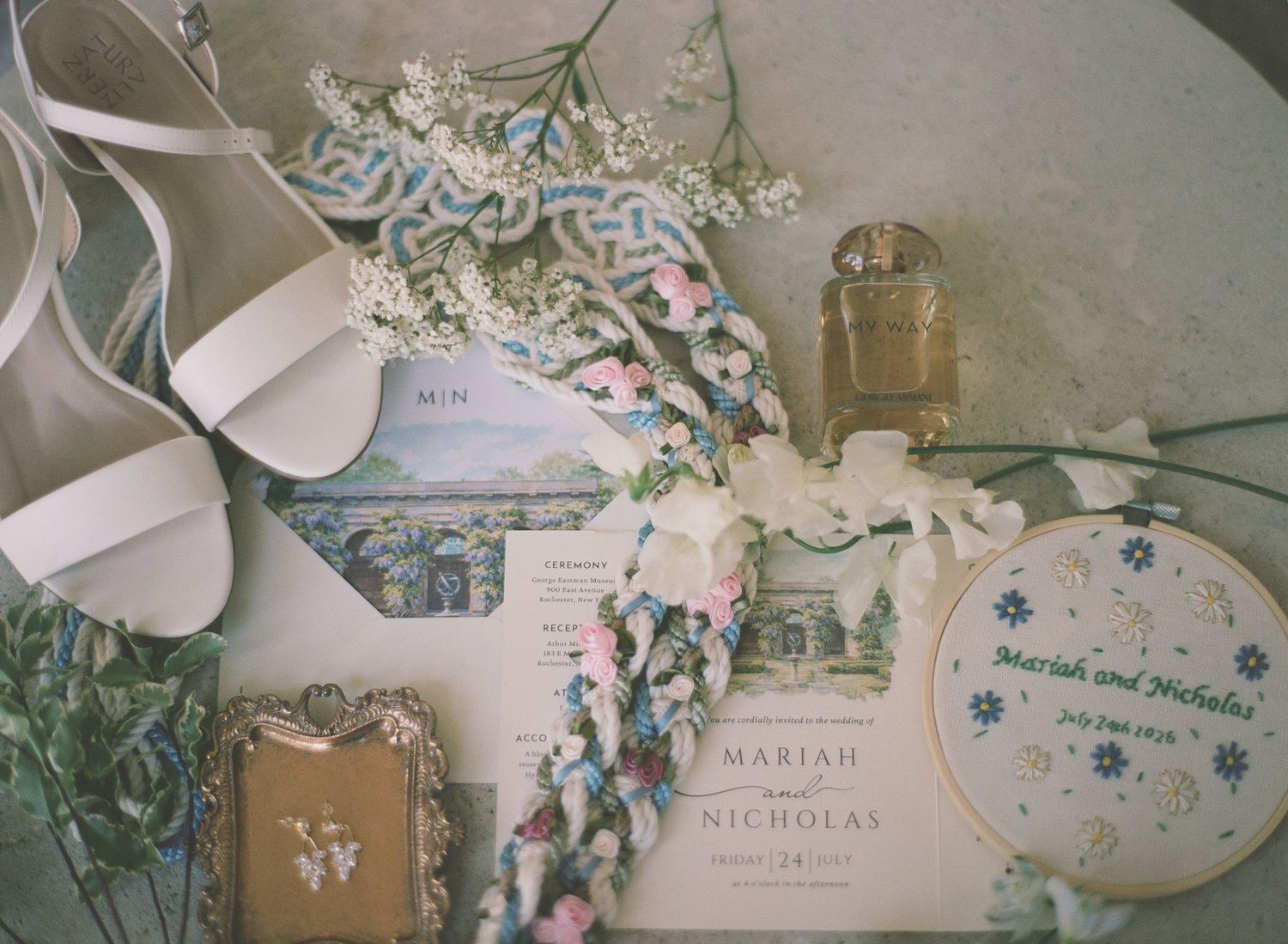Elegant wedding flat lay with white heels, floral invitation suite, embroidery hoop, vintage frame, and delicate flowers.