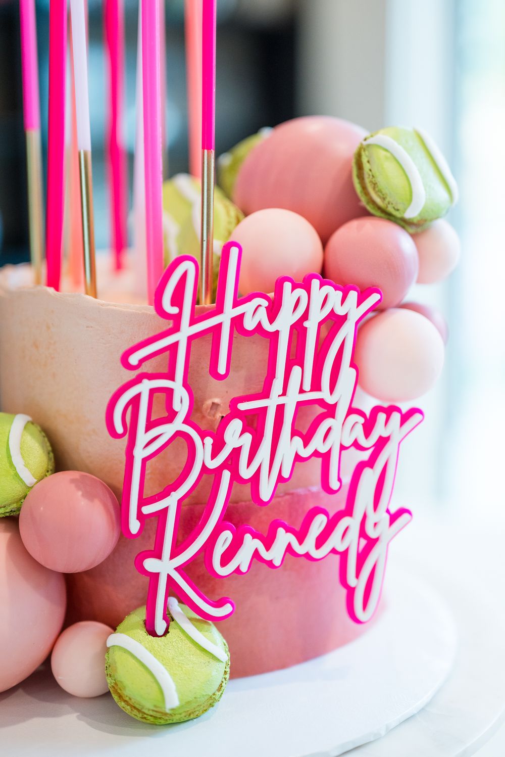 Pink birthday cake decorated with macarons and neon birthday message topper.
