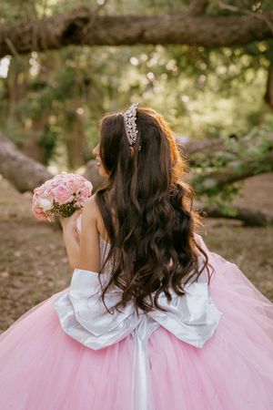 Back view of a pink princess gown with white bow detail in a forest setting.