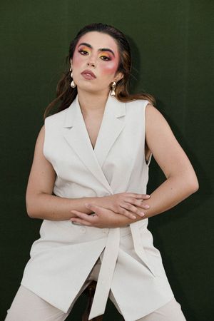 Fashion portraits in a white sleeveless blazer against a dark green background.