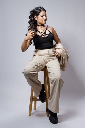 Modern fashion poses on a wooden chair wearing khaki pants and black top.