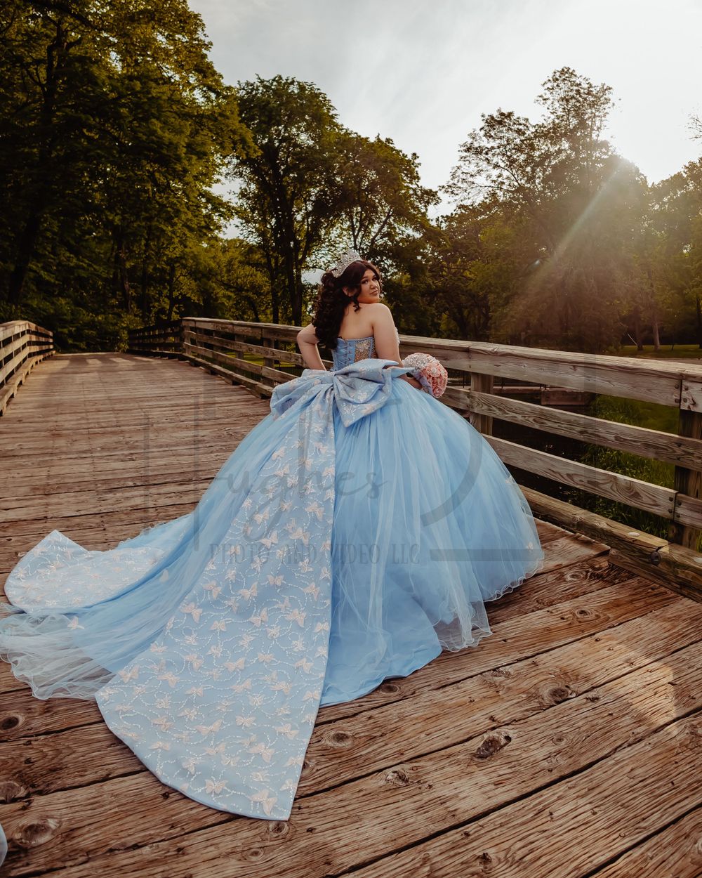 A dramatic light blue ballgown with train spreads across a wooden bridge at sunset.