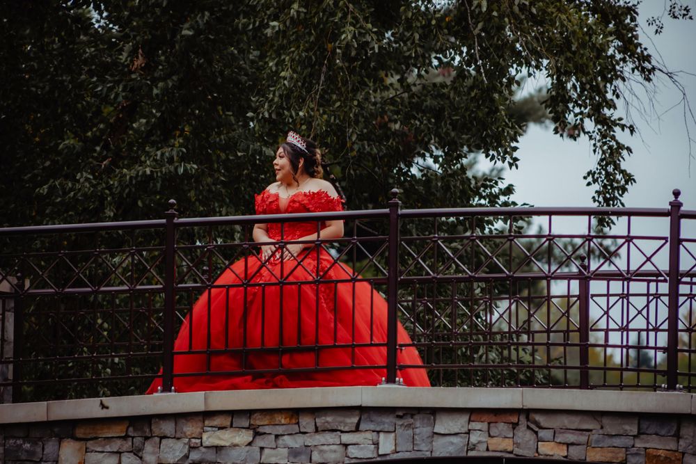 Dramatic red ball gown silhouetted against the sky on a stone bridge overlook.