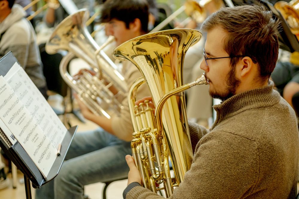 A musician playing a euphonium in a brass ensemble rehearsal, reading sheet music on a stand.