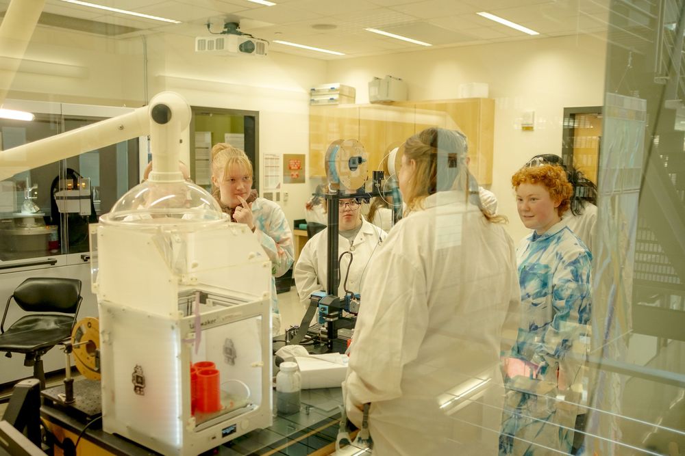 Scientists in protective suits work in a high-tech laboratory with specialized equipment and safety barriers.