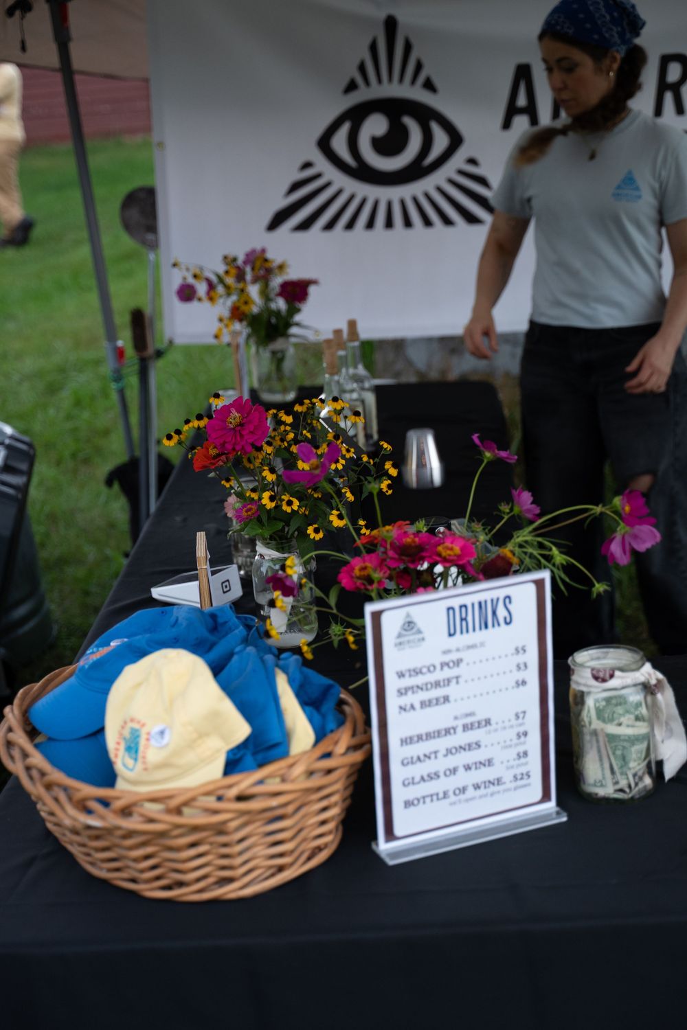 Outdoor drinks menu display with floral arrangement, wicker basket, and banner at a festival booth.