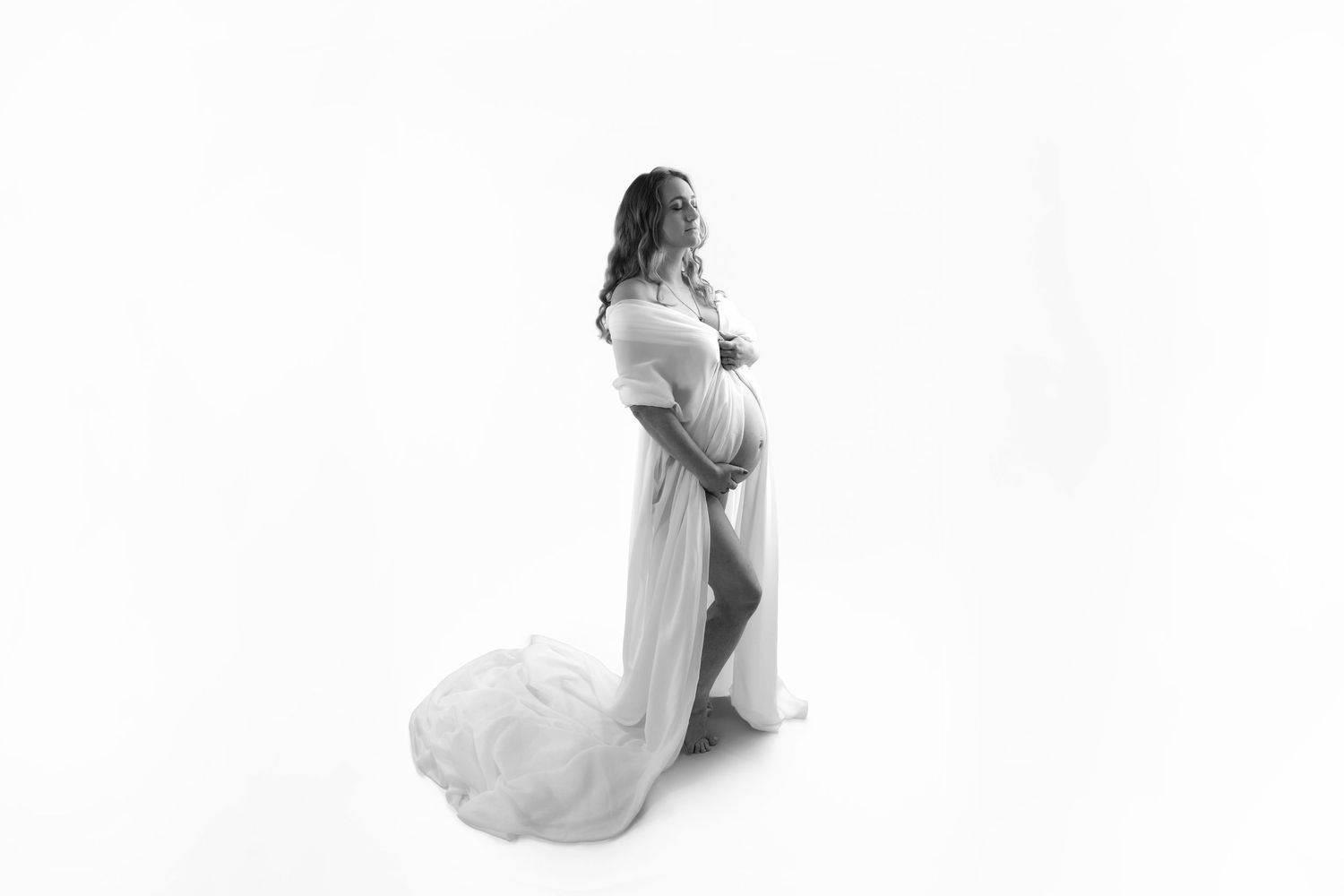 Black and white photo of a pregnant woman sitting with her toddler child, both smiling in a studio setting.