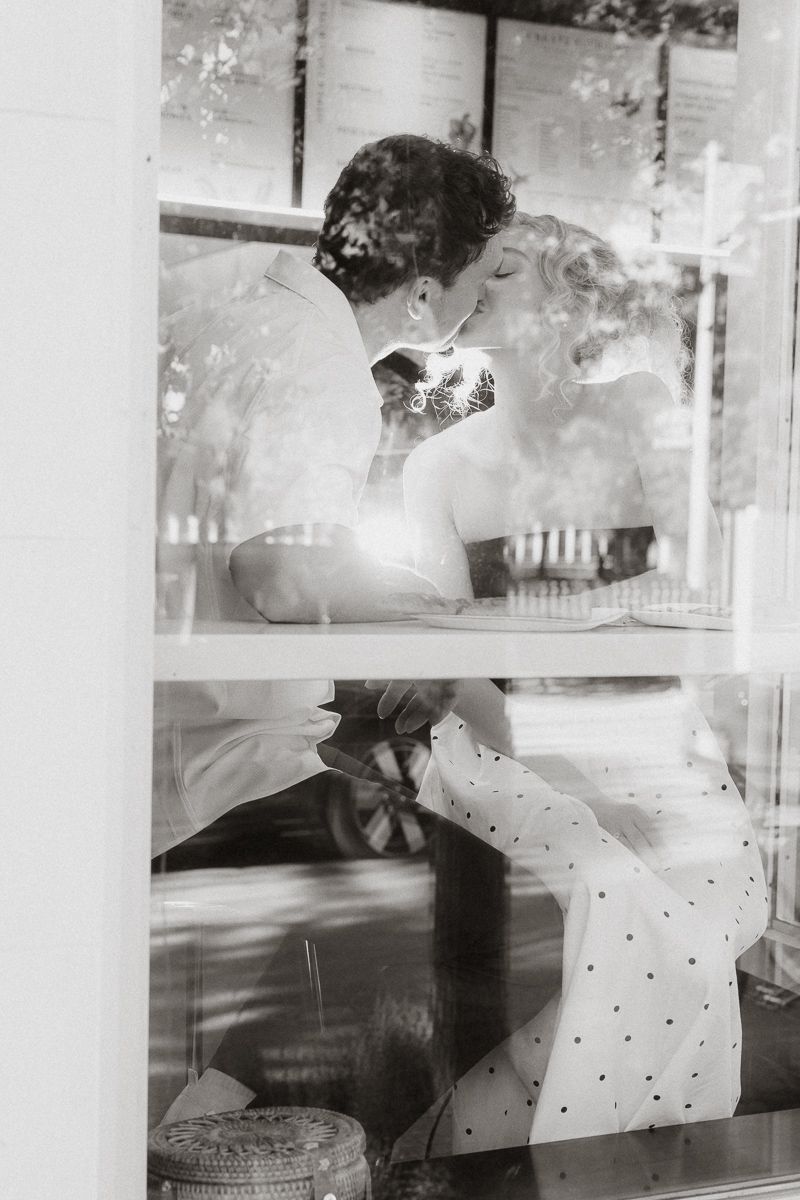 Black and white photo of a couple kissing through a window, captured in a romantic and intimate moment.