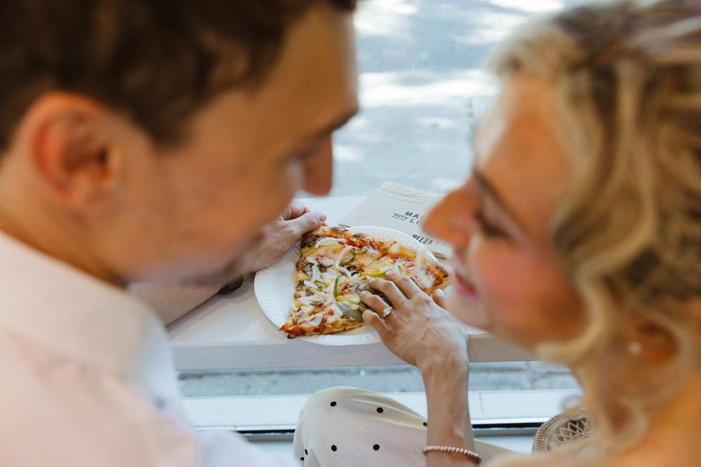 Couple sharing a slice of pizza on a white plate, enjoying a romantic meal together.