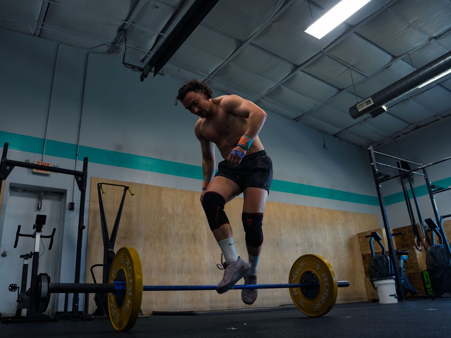 CrossFit athlete in knee sleeves hops over a loaded barbell during a bar-facing burpee at CrossFit Mojo in Madison, WI, mid-workout.