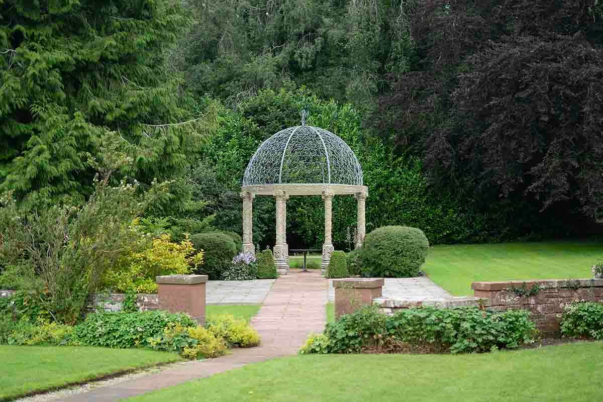 Elegant stone gazebo with domed trellis top surrounded by lush green garden landscaping and manicured lawns at Dalston Hall Wedding venue