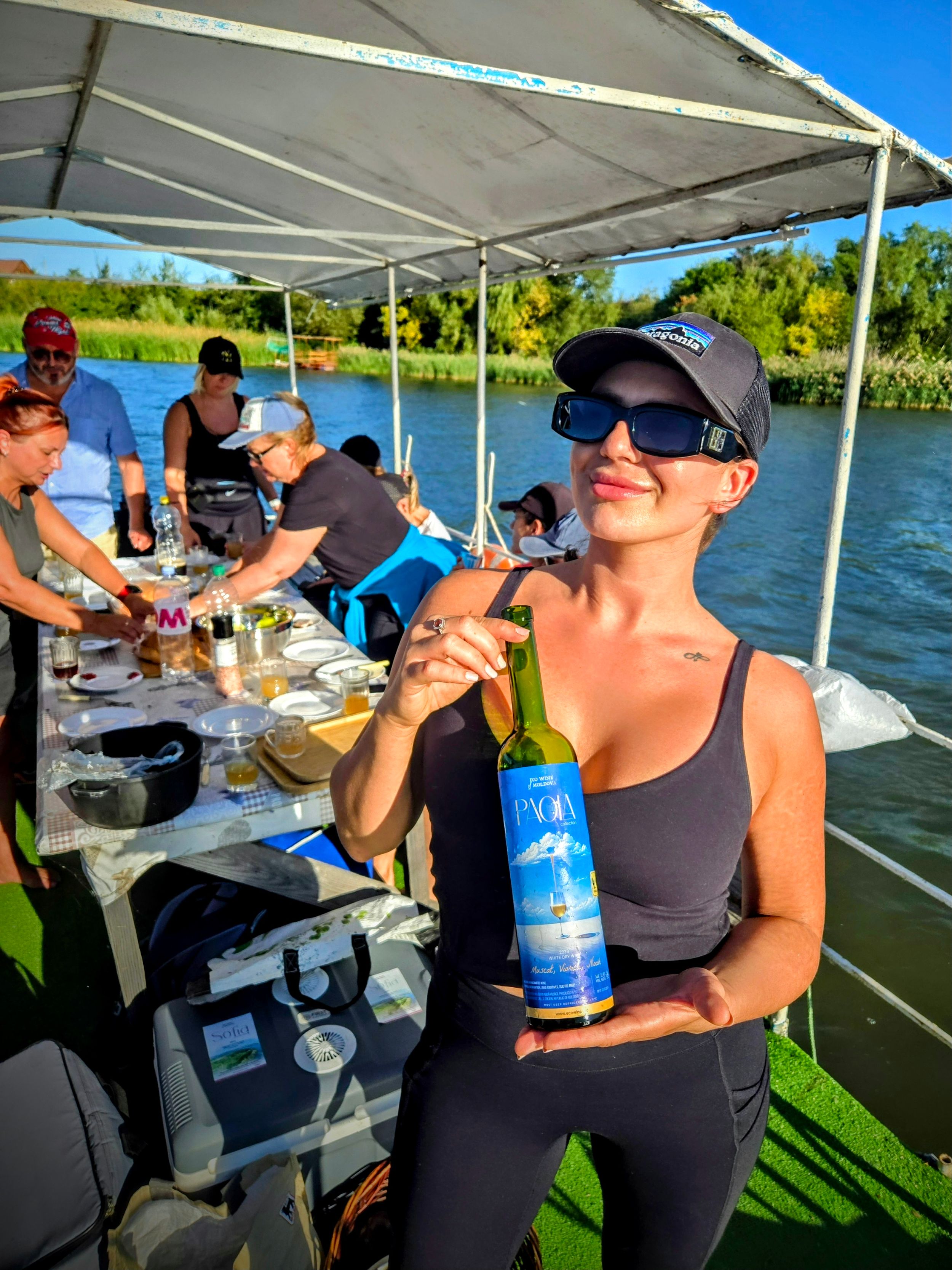Woman holding a wine bottle on a boat tour with guests dining on a river.
