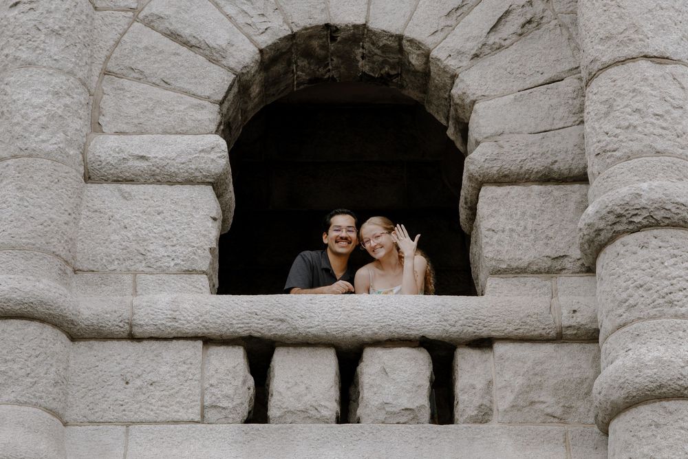 Couple smiling and waving from a stone castle window balcony.