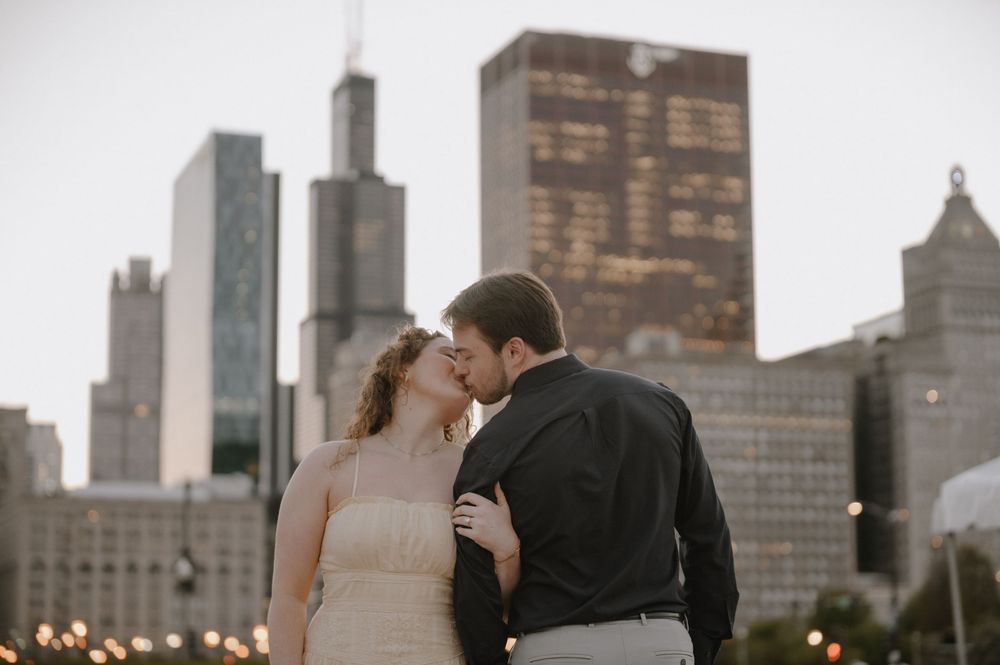 Couple sharing a romantic kiss with Chicago skyline and Willis Tower in the background at dusk.