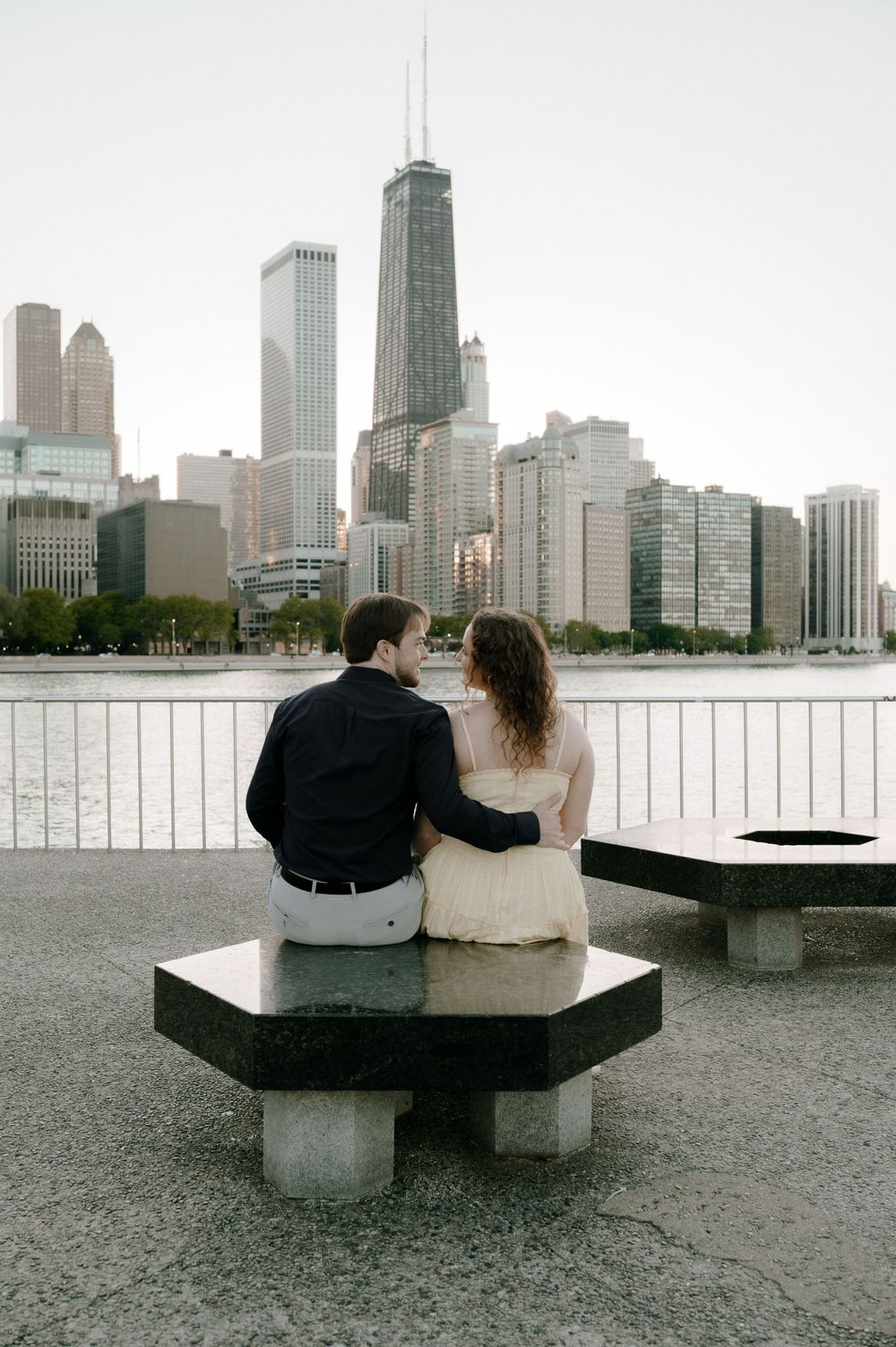 Couple sitting on a bench facing the Chicago skyline with the John Hancock Center visible across the waterfront.