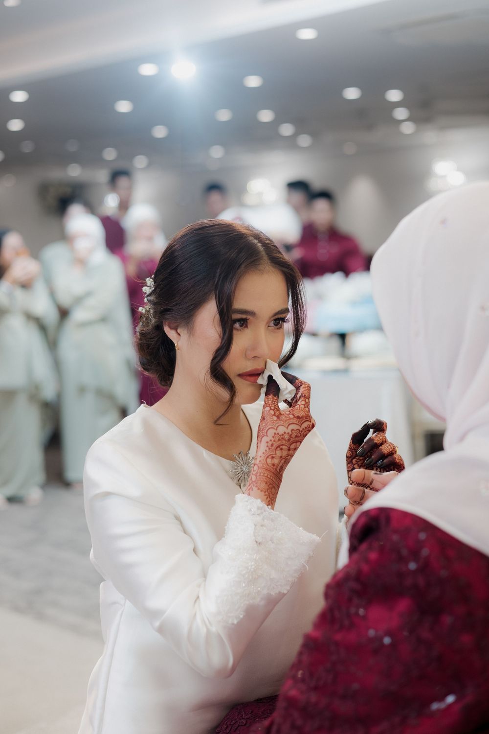 Bride in white dress gets lipstick applied by makeup artist with henna hands at a wedding ceremony.